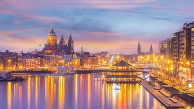 Un paisaje urbano al anochecer con una catedral destacada, un río que refleja luces y edificios modernos.