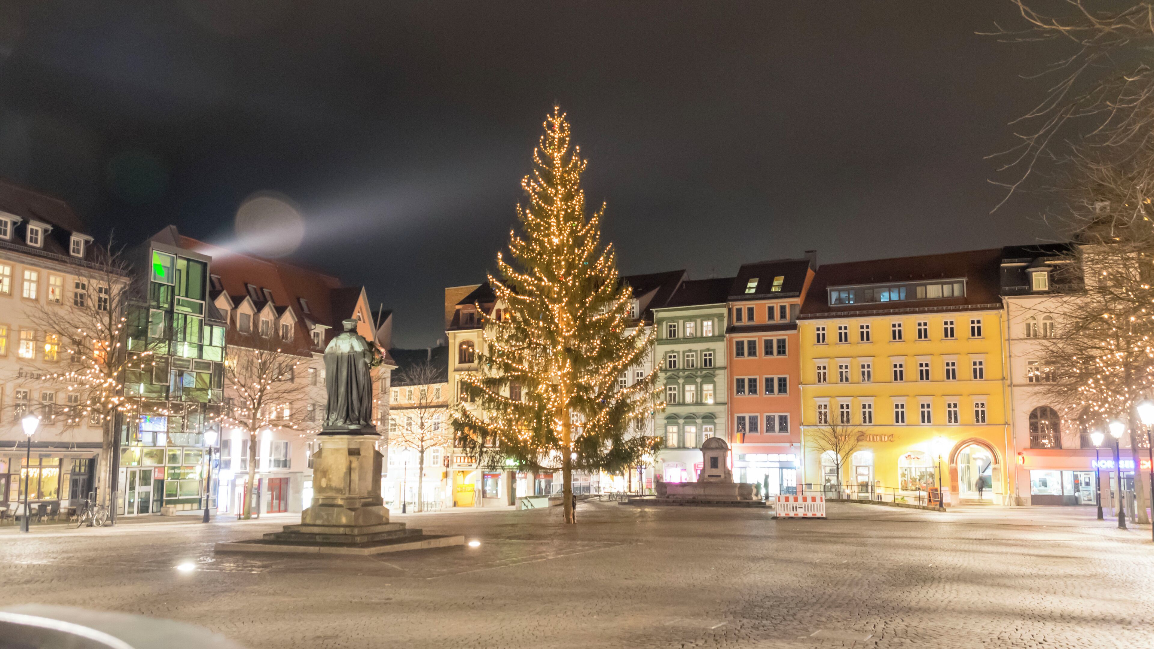 A Christmas tree in a square with buildings around.