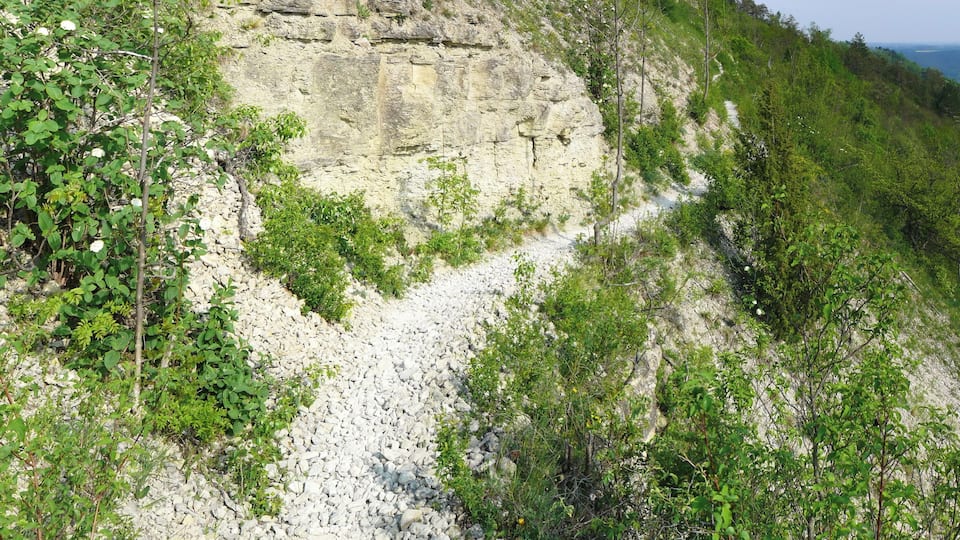 Un sendero pedregoso serpentea por una zona montañosa con poca vegetación y un cielo despejado.