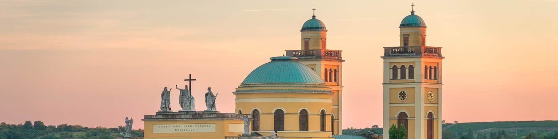 A historic church with a prominent dome and twin bell towers, surrounded by residential buildings and greenery.