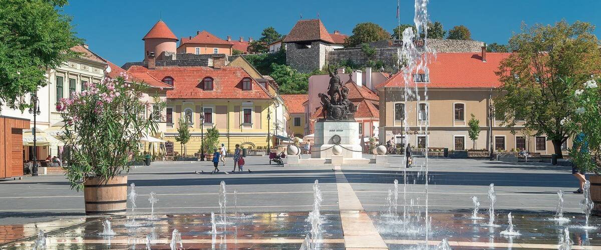 Una plaza pública con una fuente, edificios históricos y una estatua.