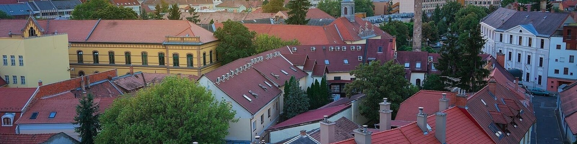 Un paisaje urbano con edificios de techos rojos, una imponente torre de iglesia y un atardecer de fondo.