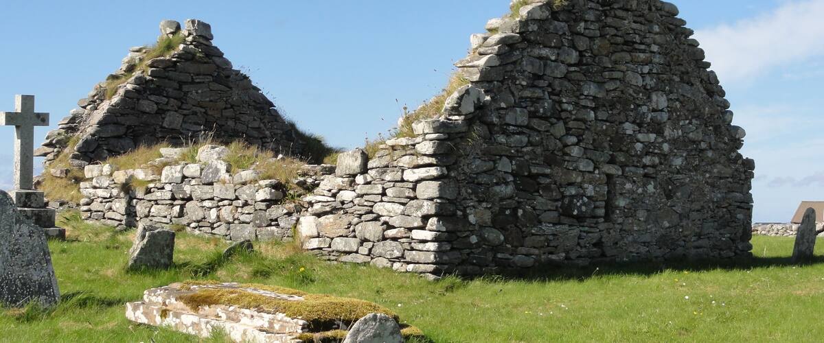 Stone ruins with thatched roofs in a grassy field.