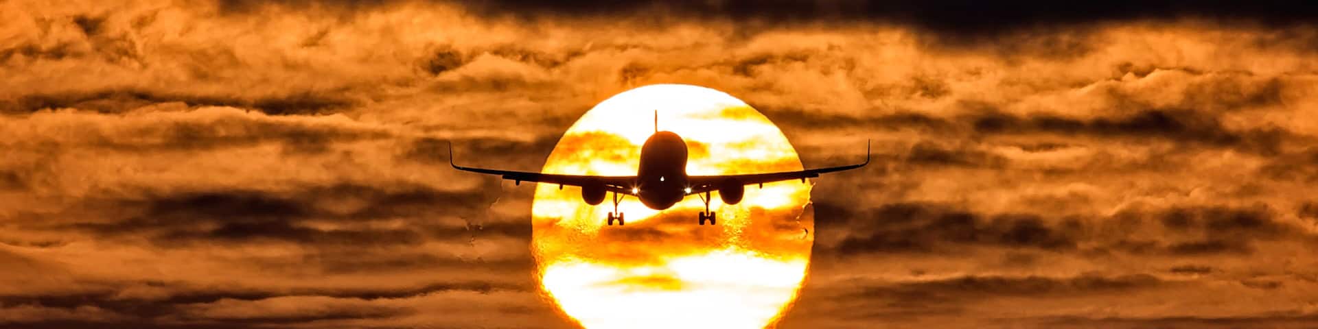 View of a silhouette airplane ascending against a fiery sunset, its wings outstretched, creating a striking contrast against the glowing sun, Schiphol, Noord-Holland, Netherlands.