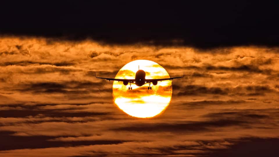 An airplane flying over a sea of clouds with a bright sun in the background.