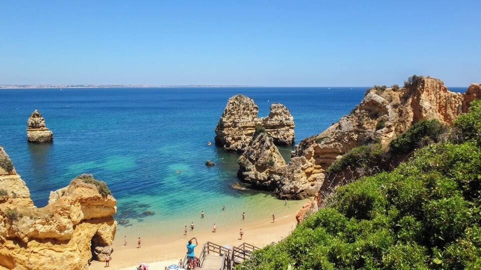 A coastal beach with rocky formations and clear blue water.