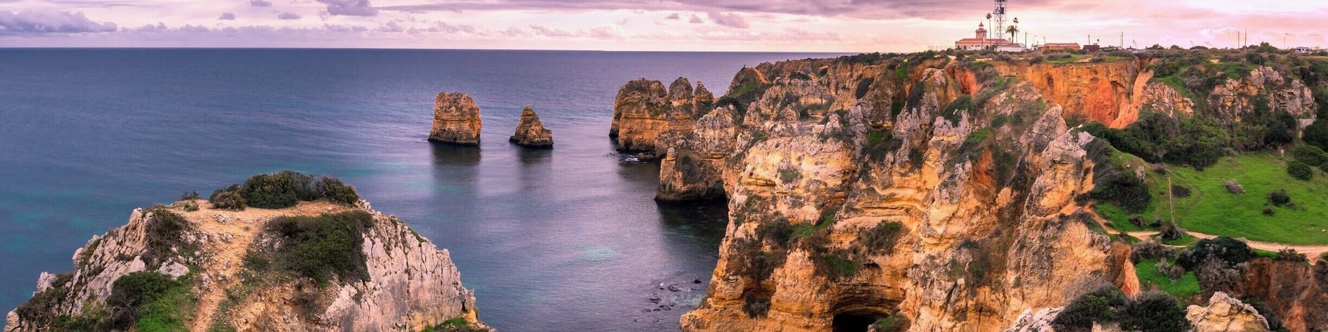 A coastal landscape with rocky cliffs, a lighthouse, and clear blue sea.