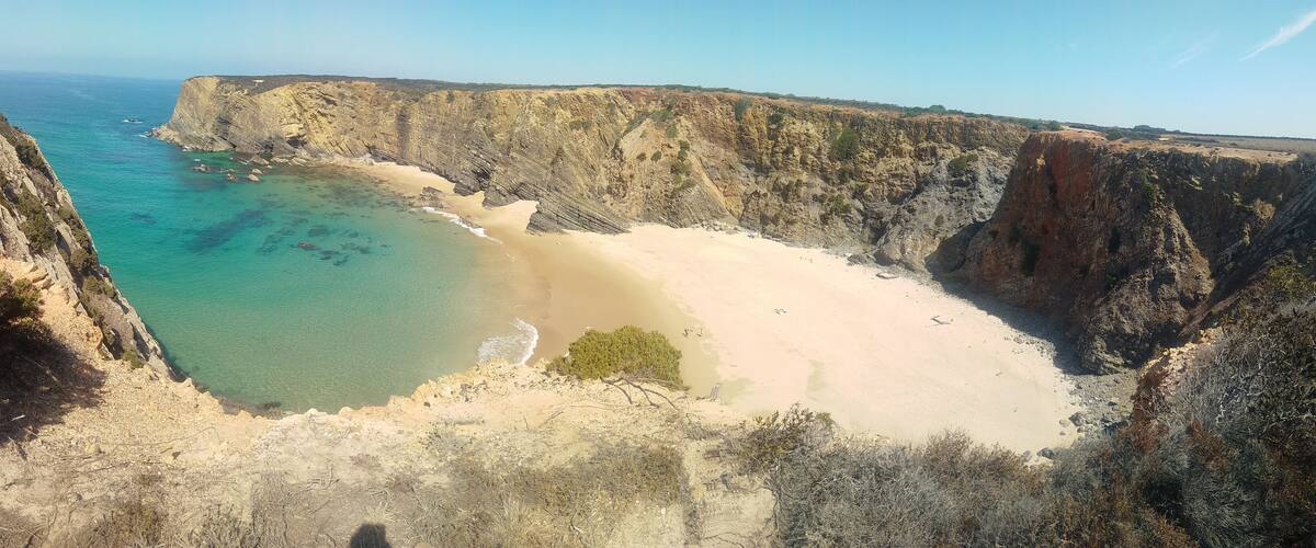 A coastal landscape with cliffs, a sandy beach, and turquoise waters.