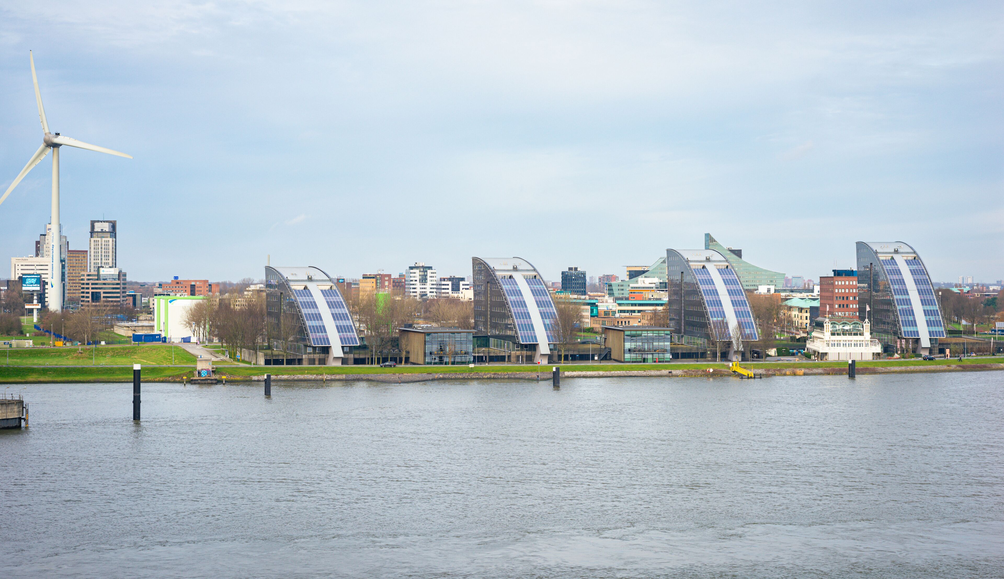 A river with modern architecture, including curved buildings and a wind turbine.