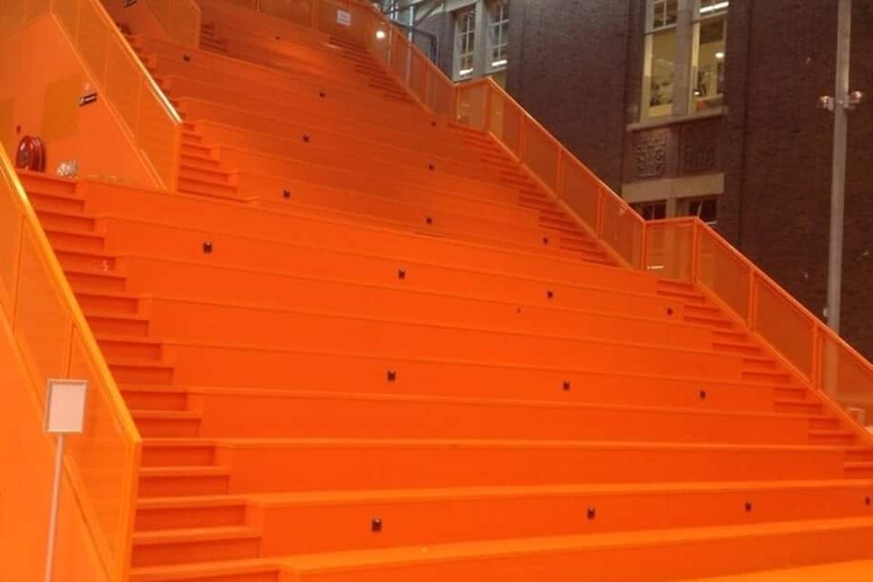 En stor, orange trappa i en industriell miljö, med metallräcken och en tegelvägg i bakgrunden.