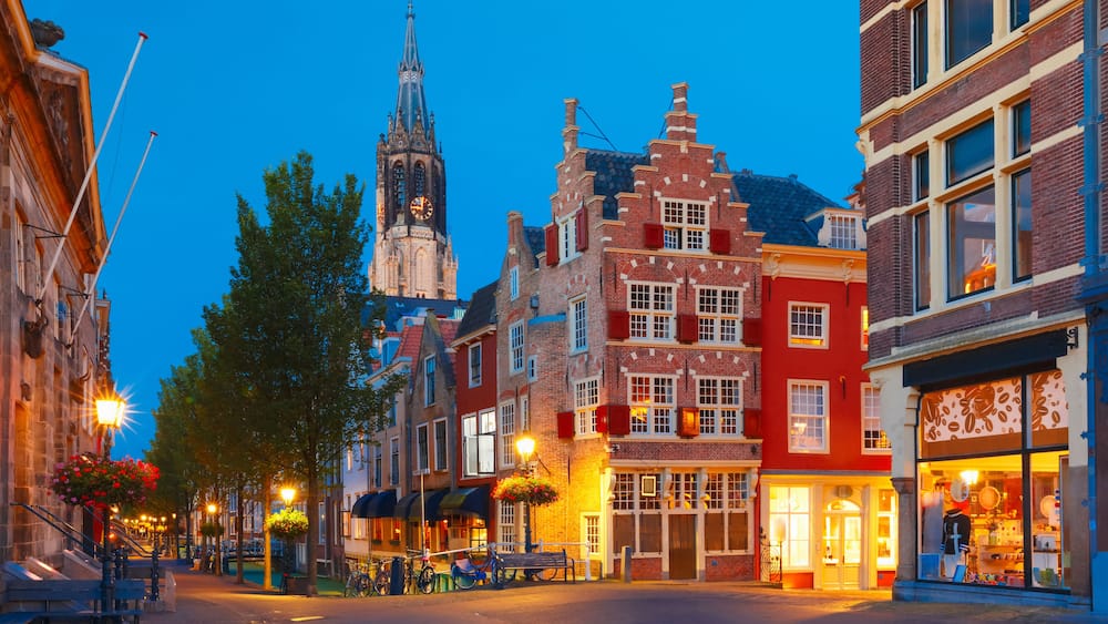 Eine historische europäische Straße mit traditioneller Architektur, einem markanten Kirchturm und einem hell erleuchteten Geschäft.