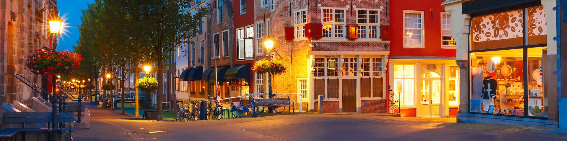 A historic European street with traditional architecture, a prominent church tower, and a brightly lit shop.