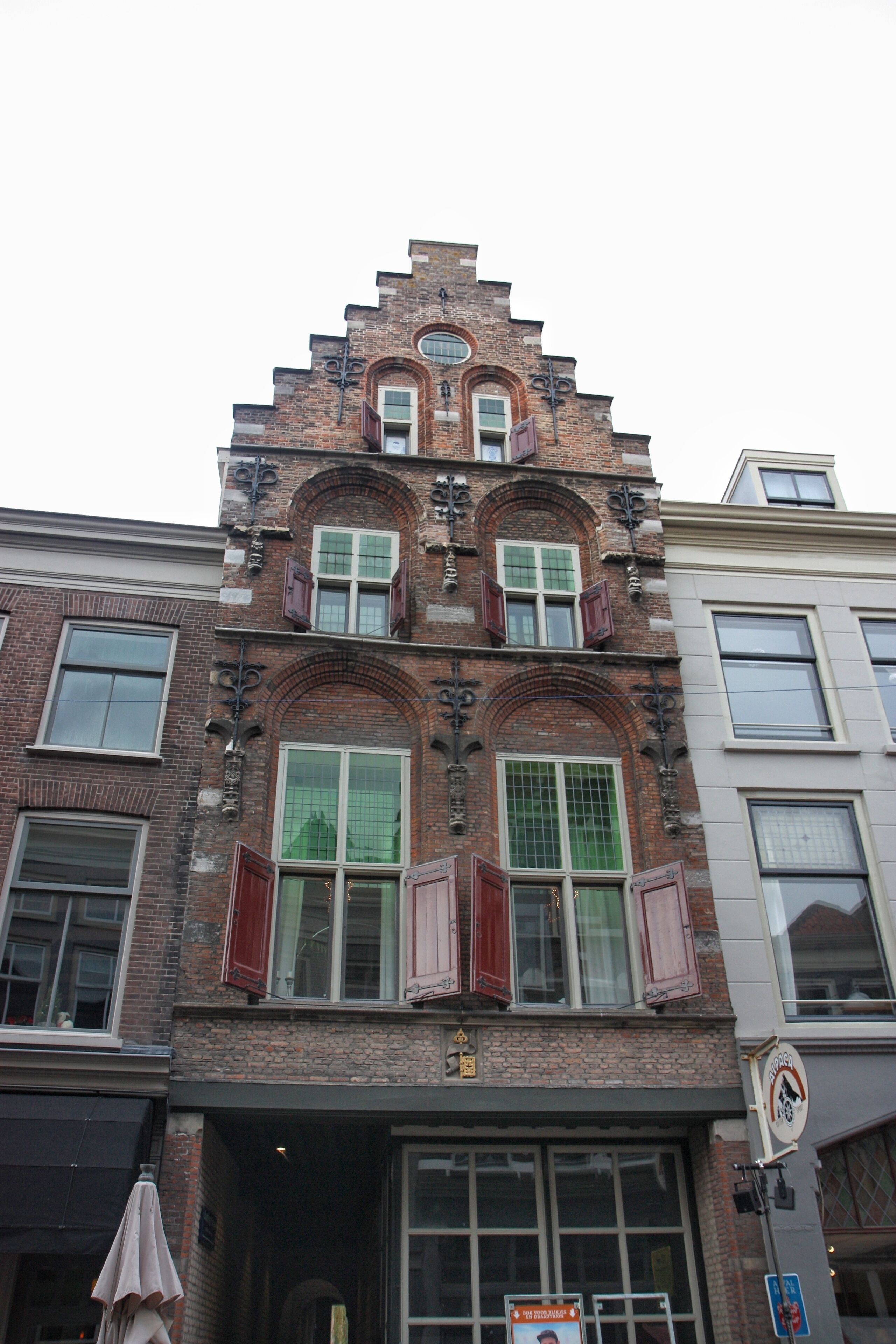 Un edificio histórico con un tejado empinado, detalles de ladrillo ornamentales y contraventanas rojas.