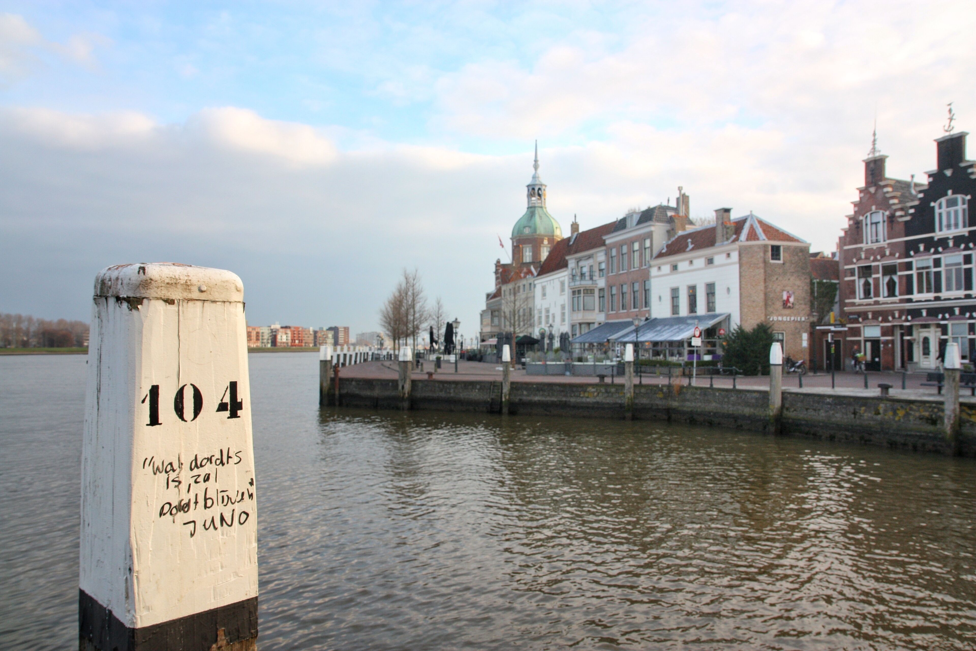 A waterfront with a sign reading "104" and historic buildings in the background.