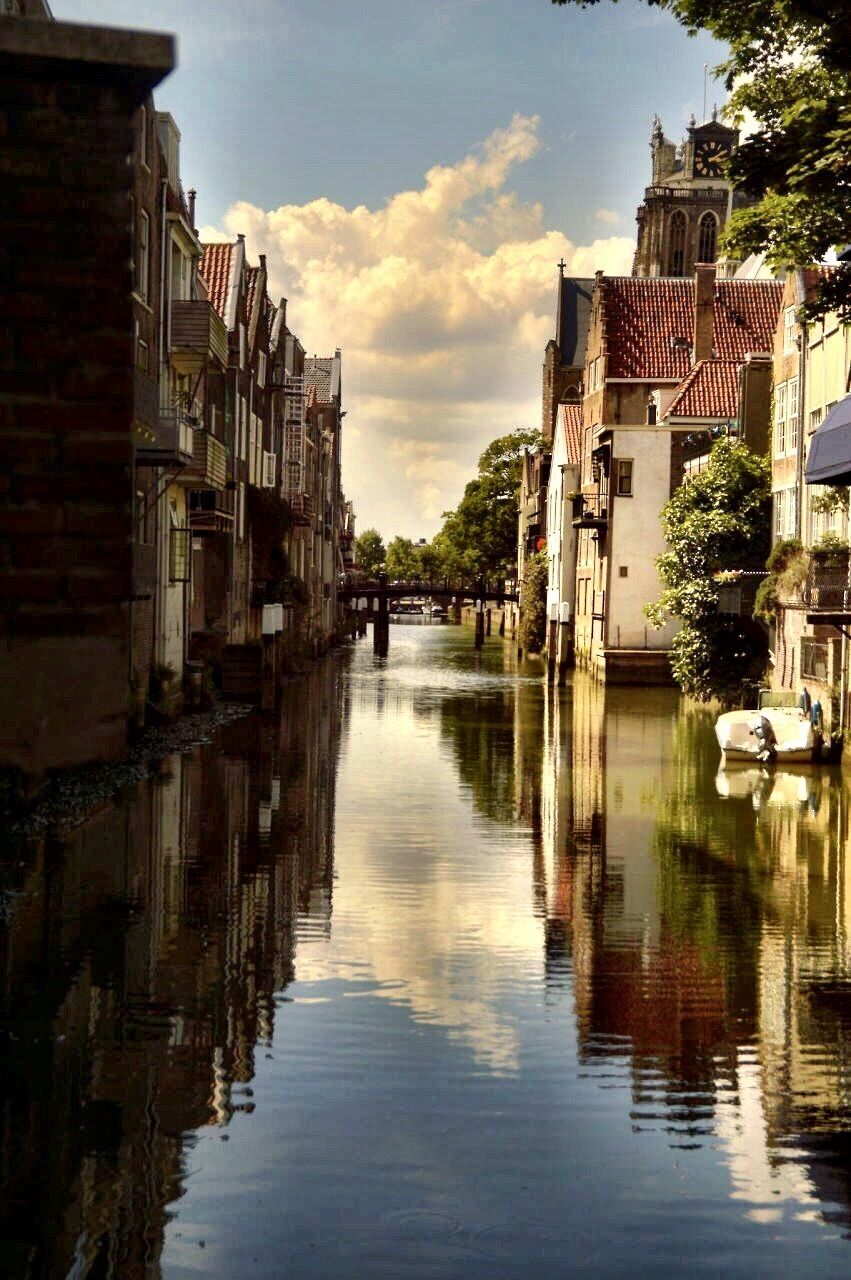 A canal with buildings on either side, a bridge in the distance, and a clock tower.
