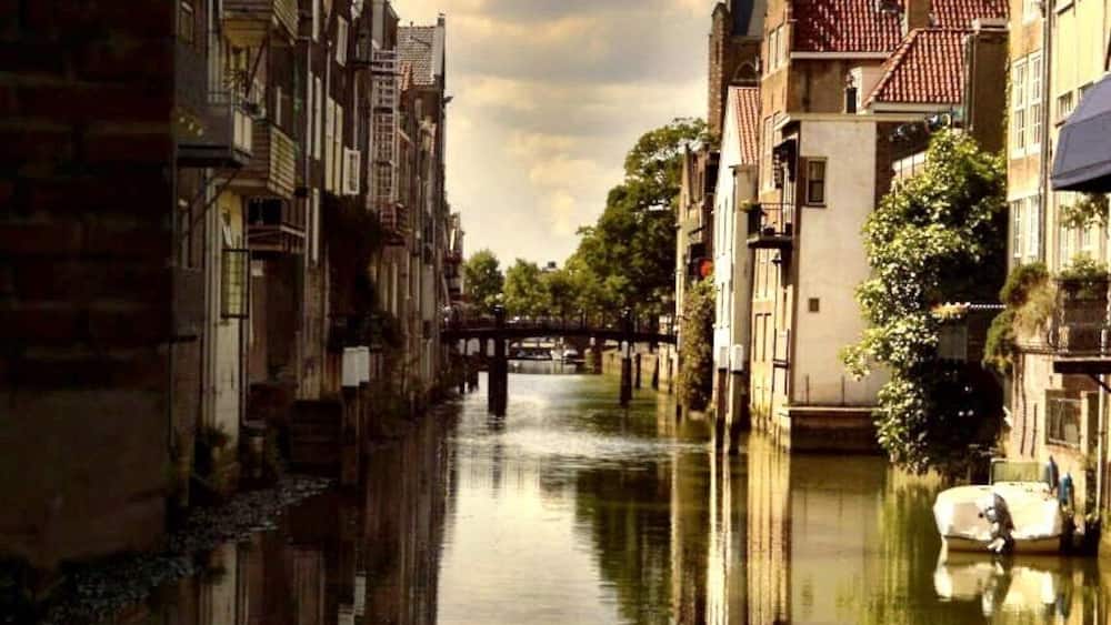 A canal with buildings on either side, a bridge in the distance, and a clock tower.