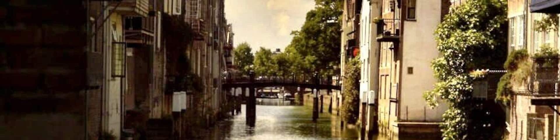 A canal with buildings on either side, a bridge in the distance, and a clock tower.