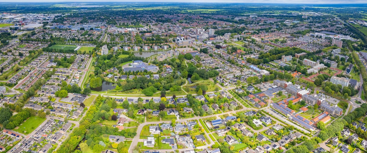 An aerial view of a city with dense residential areas, green spaces, and a large central park with a lake.