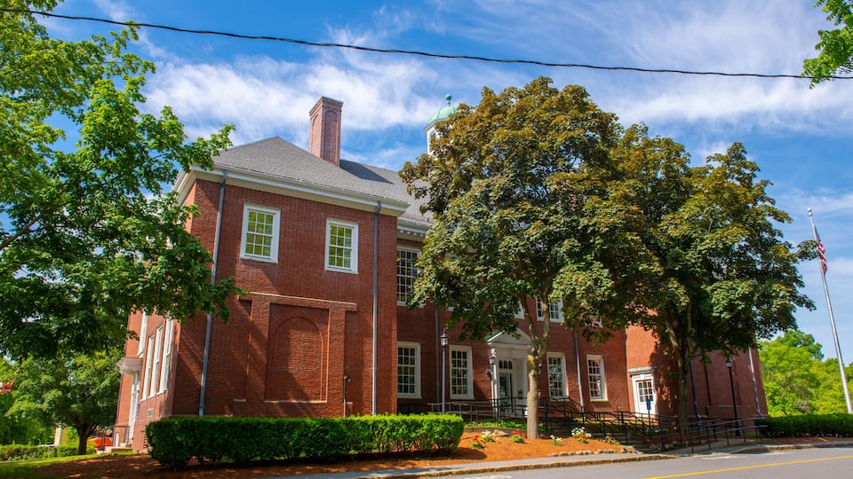 A red brick building with a white door, surrounded by trees and a clear blue sky.