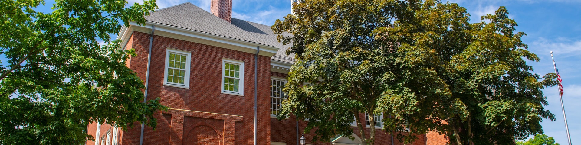 A red brick building with a white door, surrounded by trees and a clear blue sky.