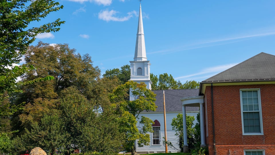 A church with a tall steeple, surrounded by trees and a brick building.