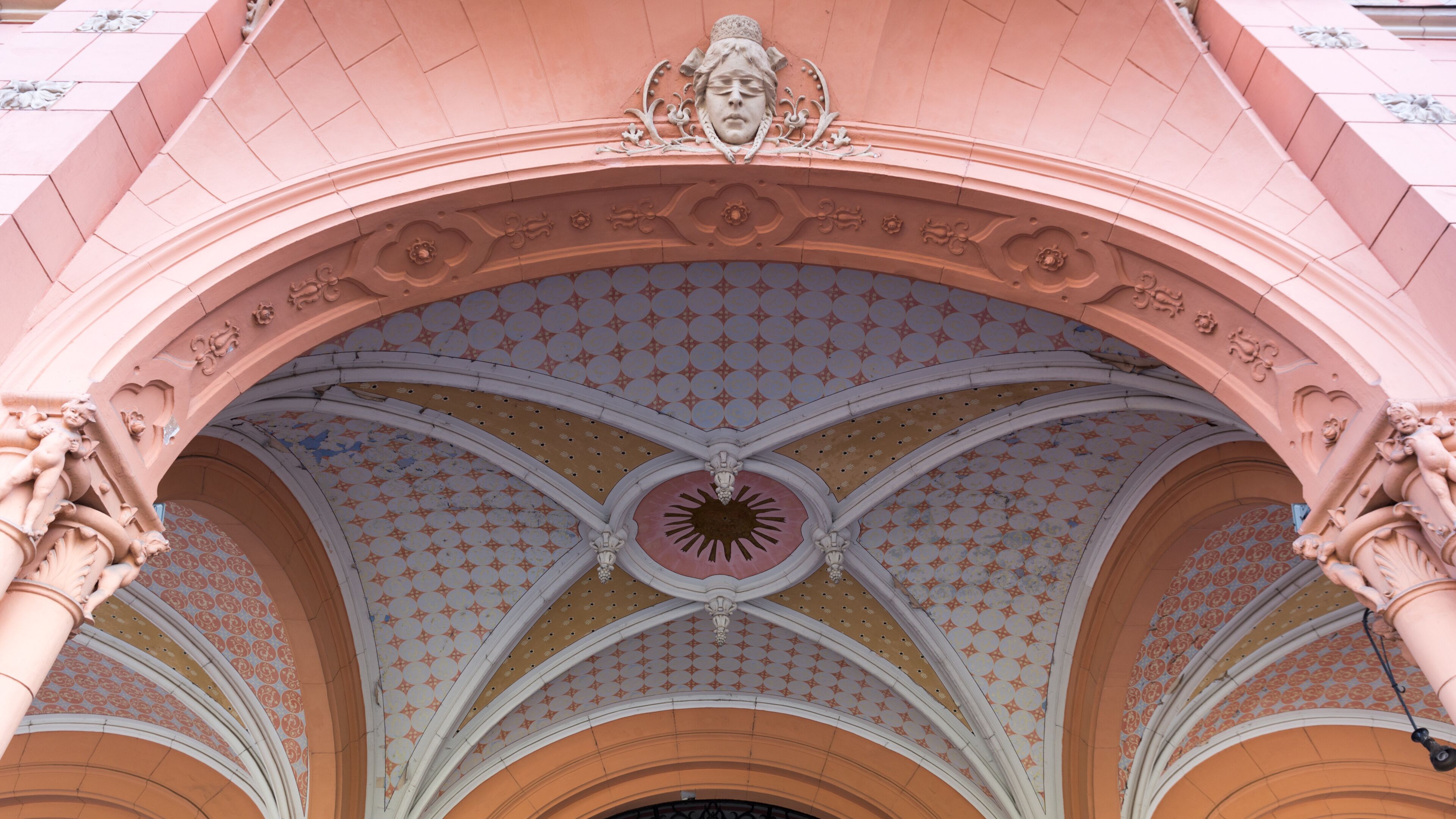 A pink arched ceiling with a sunburst design and decorative statues.