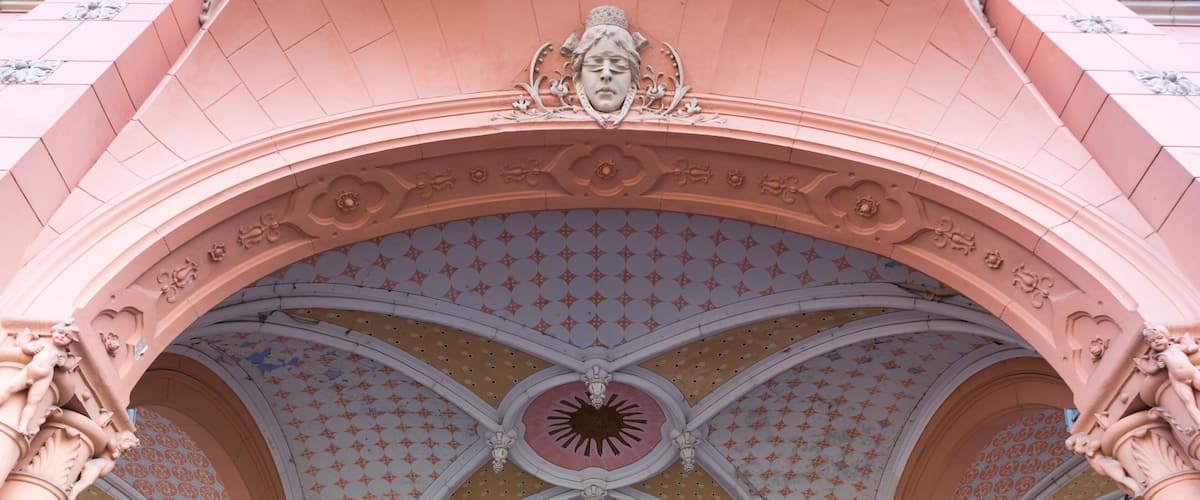 A pink arched ceiling with a sunburst design and decorative statues.