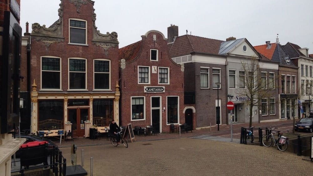 Une rue pavée bordée de bâtiments historiques, un vélo et une enseigne indiquant « Planétarium ».