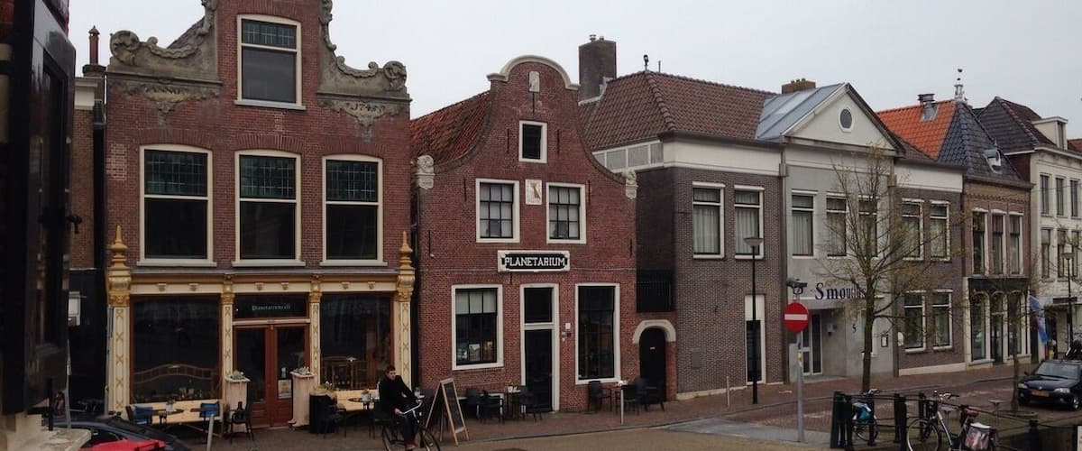A cobblestone street with historic buildings, a bicycle, and a 'Planetarium' sign.