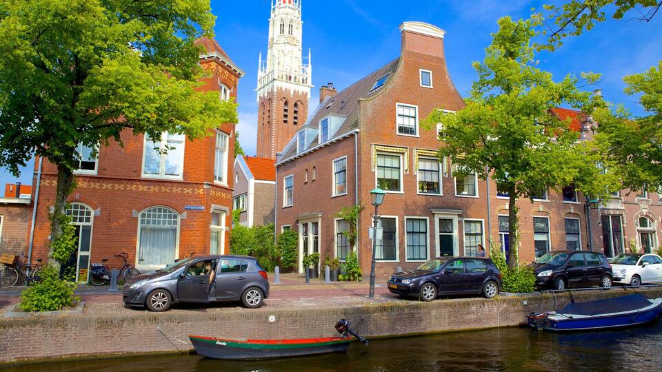 A canal with boats, a car, and historic buildings with a church tower.