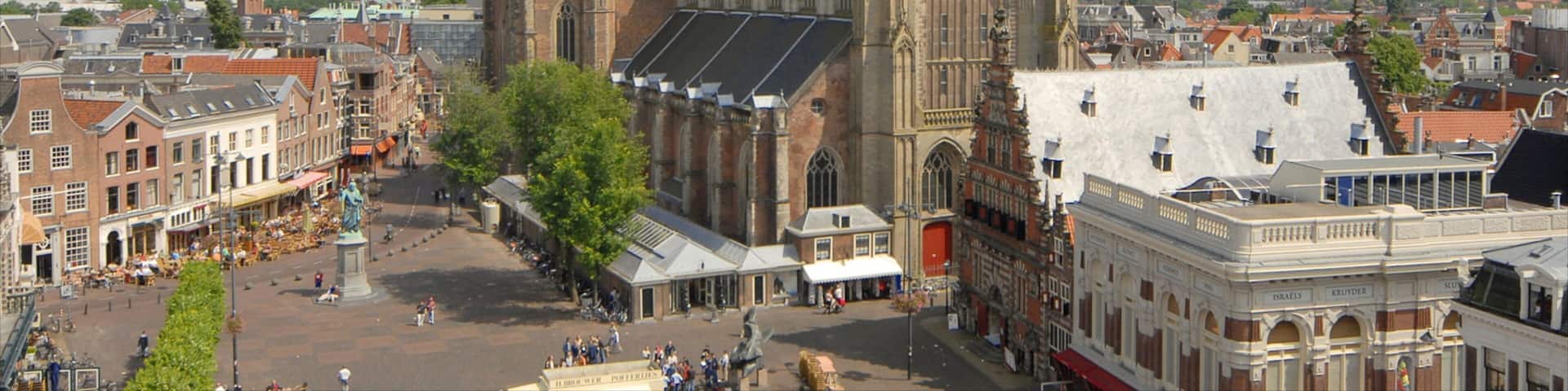 A historic church with a tall spire and a clock tower, surrounded by a bustling square with cafes and pedestrians.