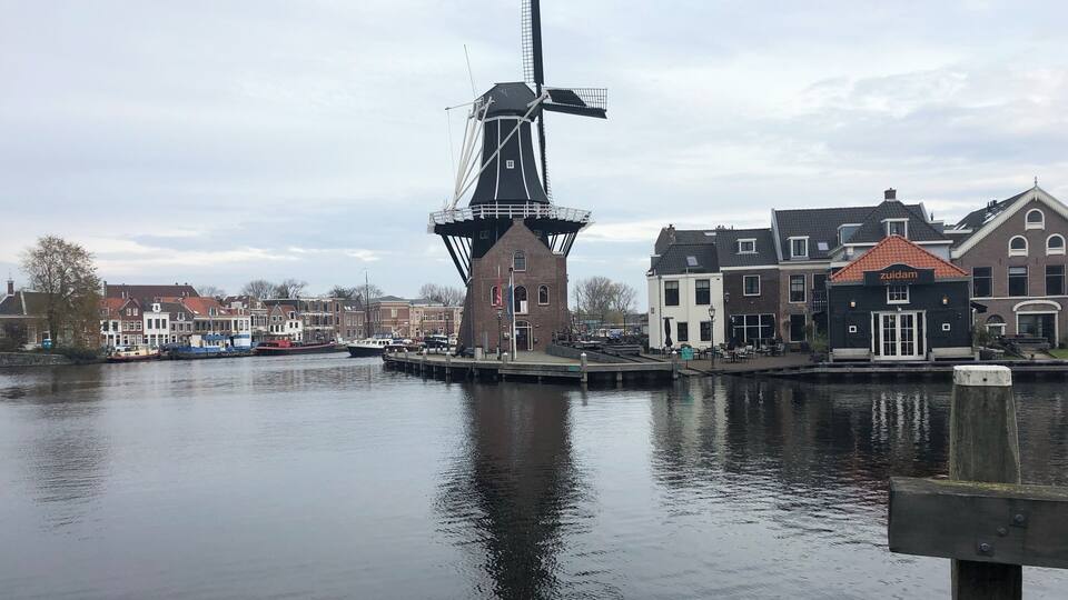 A traditional windmill by a calm river, surrounded by historic buildings.
