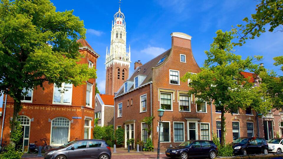 A historic town with red brick buildings, a prominent church tower, and lush green trees.