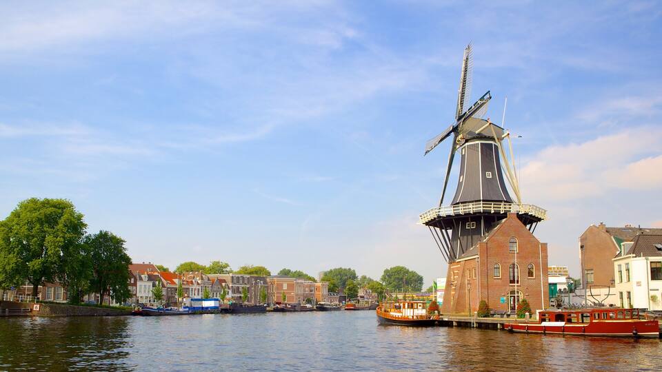 A traditional windmill by a canal with boats and historic buildings in the background.