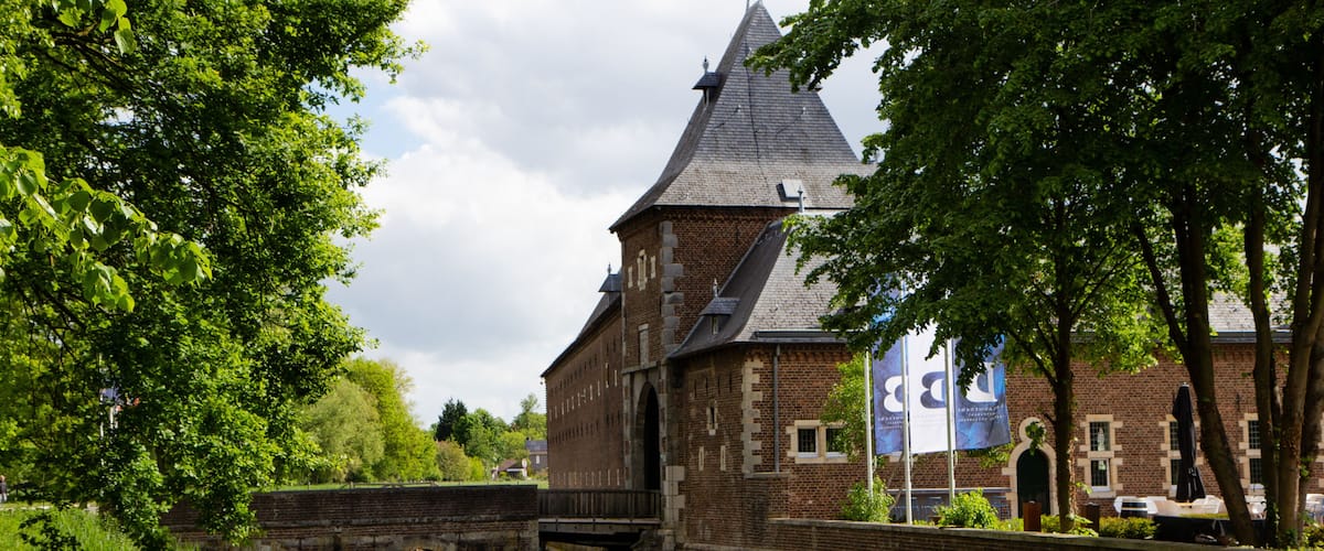 A canal with a bridge, a brick building with a pointed roof, and lush green trees.