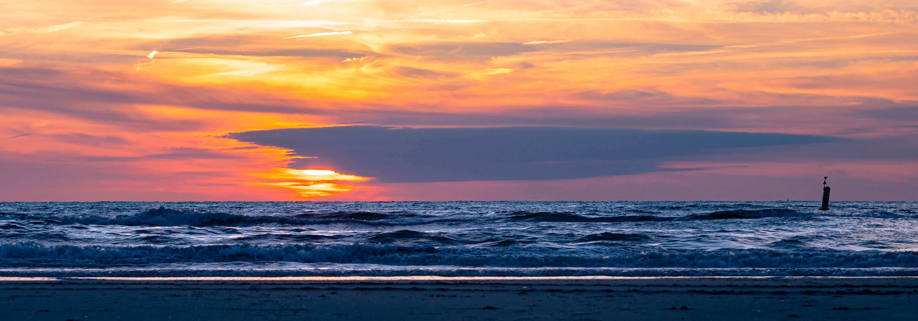 A sunset over the ocean with waves and a lighthouse.