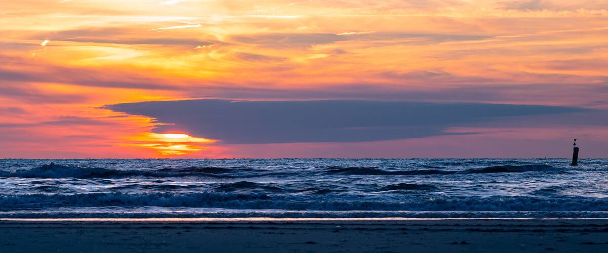 A sunset over the ocean with waves and a lighthouse.