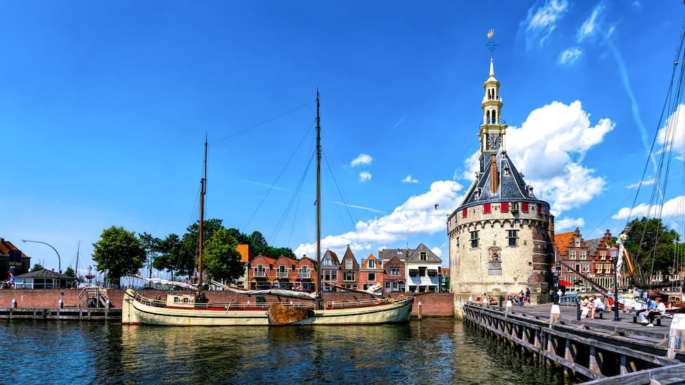 Une tour historique dotĂ©e dâune horloge, un bateau traditionnel amarrĂ© Ă un quai et une promenade en bord de mer bordĂ©e de bĂątiments.