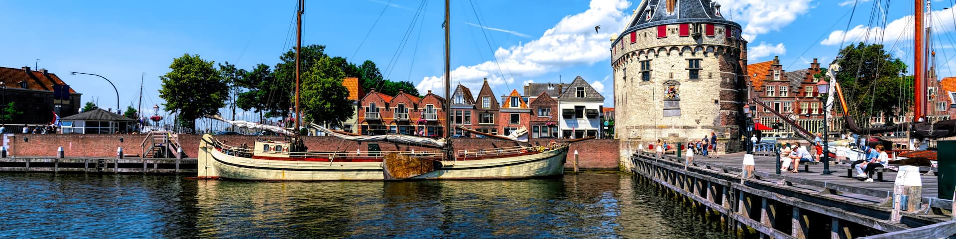 A historic tower with a clock, a traditional boat docked at a pier, and a waterfront with buildings.