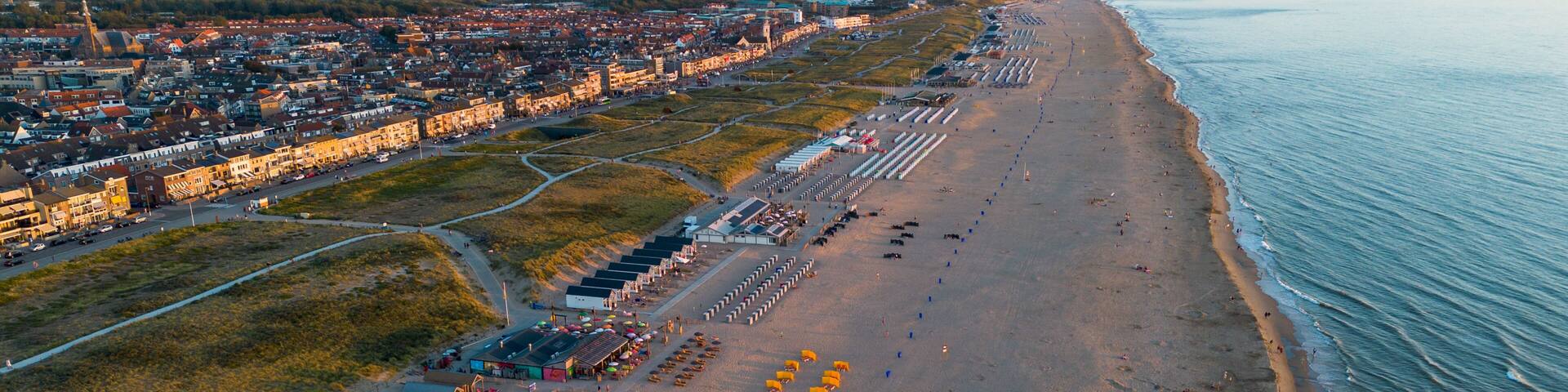 Beautiful flight in summer over the beach in Katwijk aan Zee. People are resting near the sea. Houses for tourists. Beach umbrellas, rides, people swimming in the sea. Beach in Netherland. North Sea.