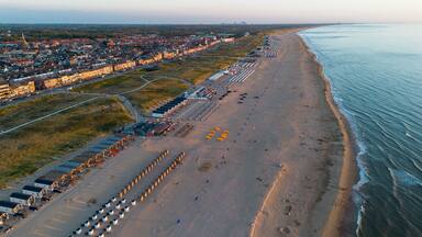 An aerial view of a coastal city with a long beachfront, a dense urban area with historic buildings, and a clear sky.