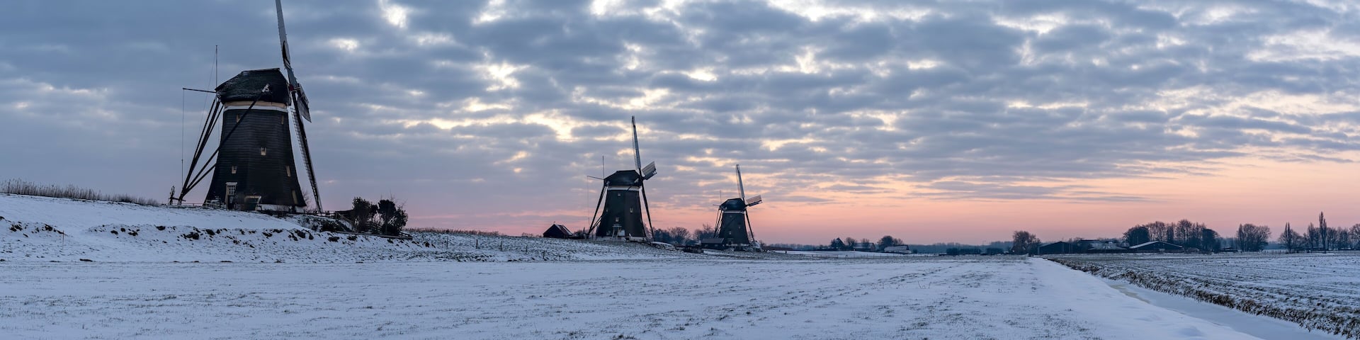 Panorama photo of a sunrise on a cold winter morning with a snowy landscape at the three windmills in Leidschendam, The Netherlands