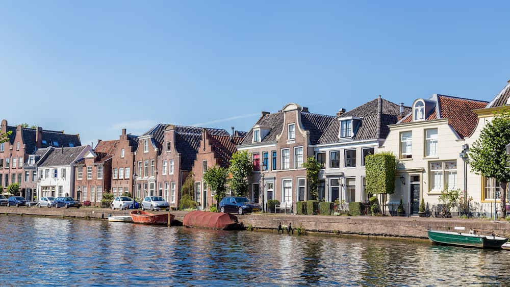 A canal with boats, a row of traditional houses, and a clear blue sky.