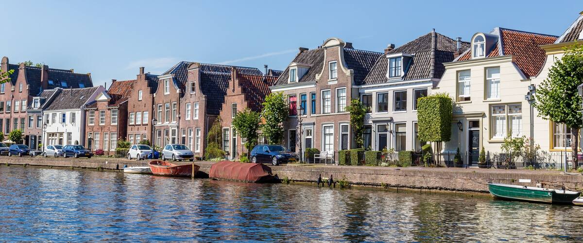 A canal with boats, a row of traditional houses, and a clear blue sky.