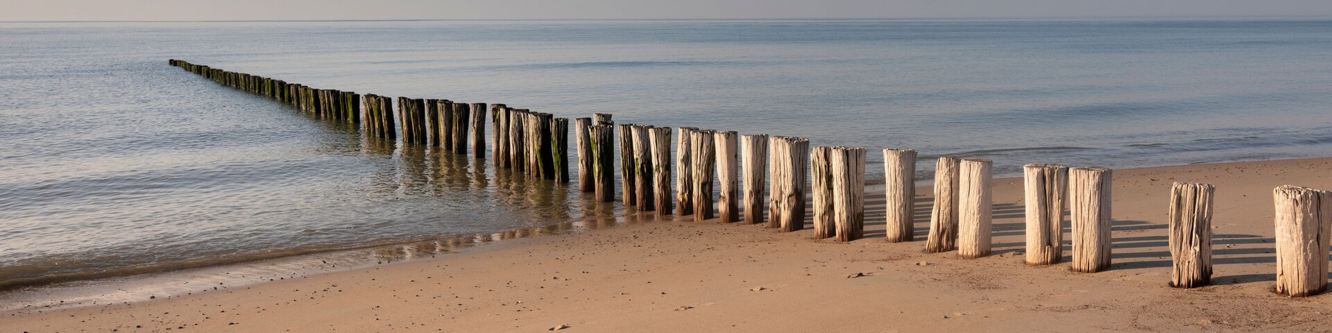 A sandy beach with a wooden groyne extending into the water.