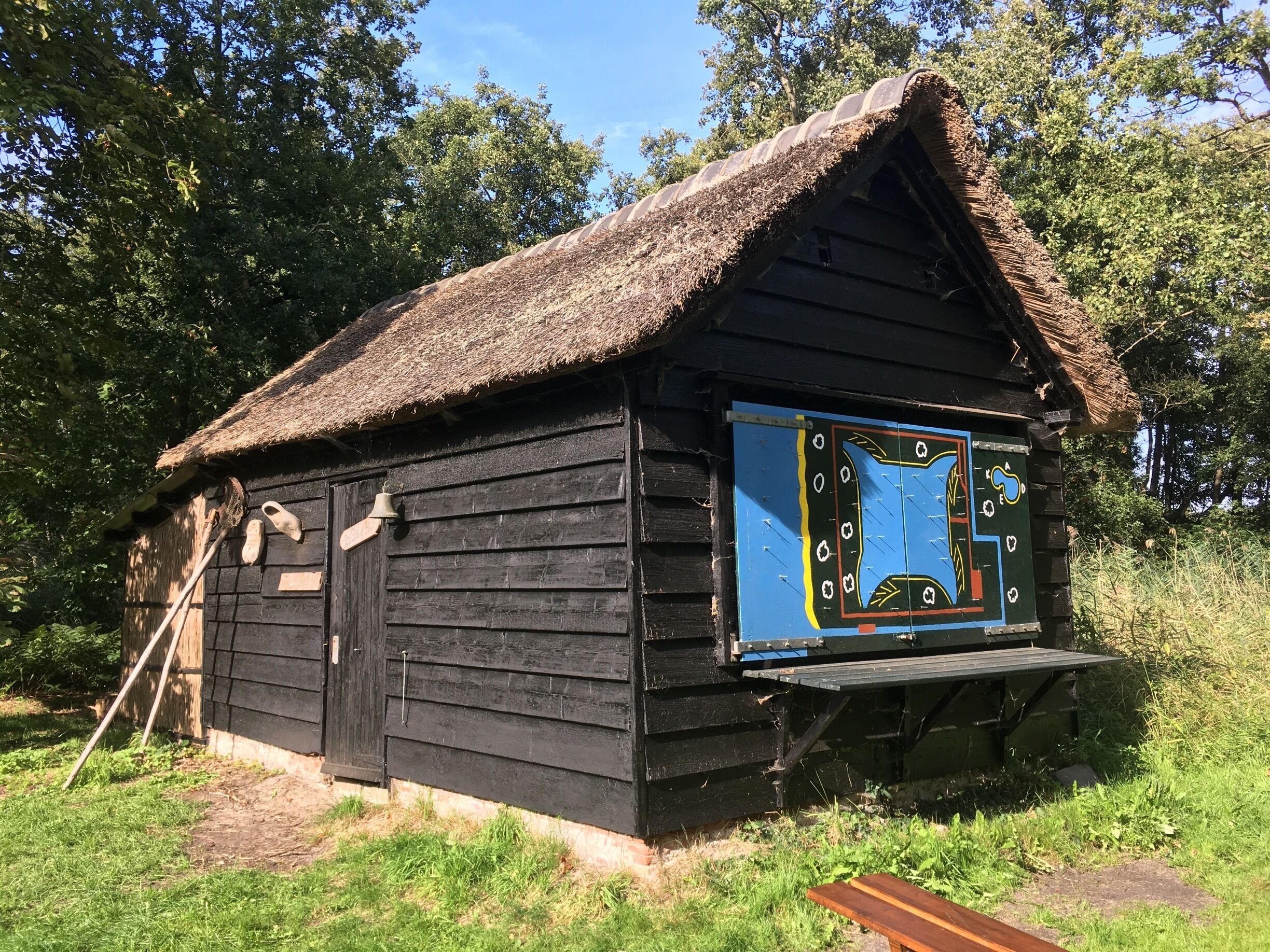 A rustic wooden cabin with a thatched roof, a wooden bench, and a colorful signboard.