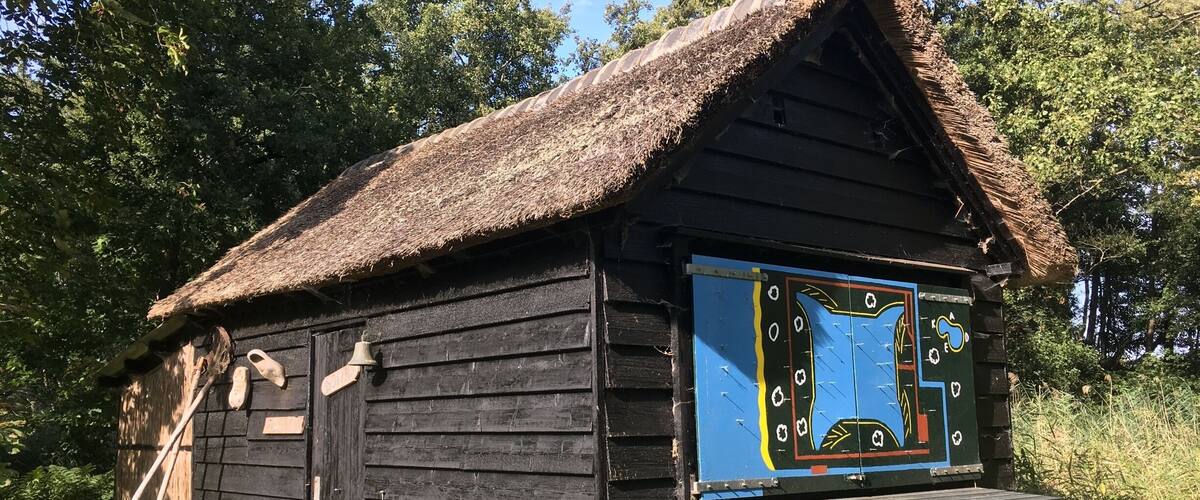 A rustic wooden cabin with a thatched roof, a wooden bench, and a colorful signboard.