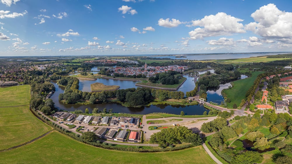 Aerial 360 panoramic view on the fortification city Naarden Vesting below a cloud with its defensive constructions surrounding the village against a blue sky with clouds passing