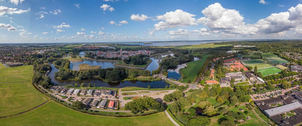An aerial view of a town with a river, green fields, and a sports complex.