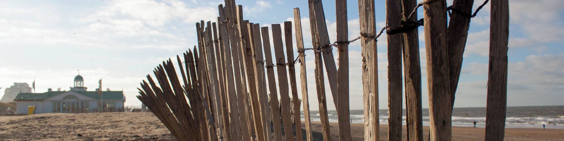 A wooden fence on a sandy beach with a building in the background.